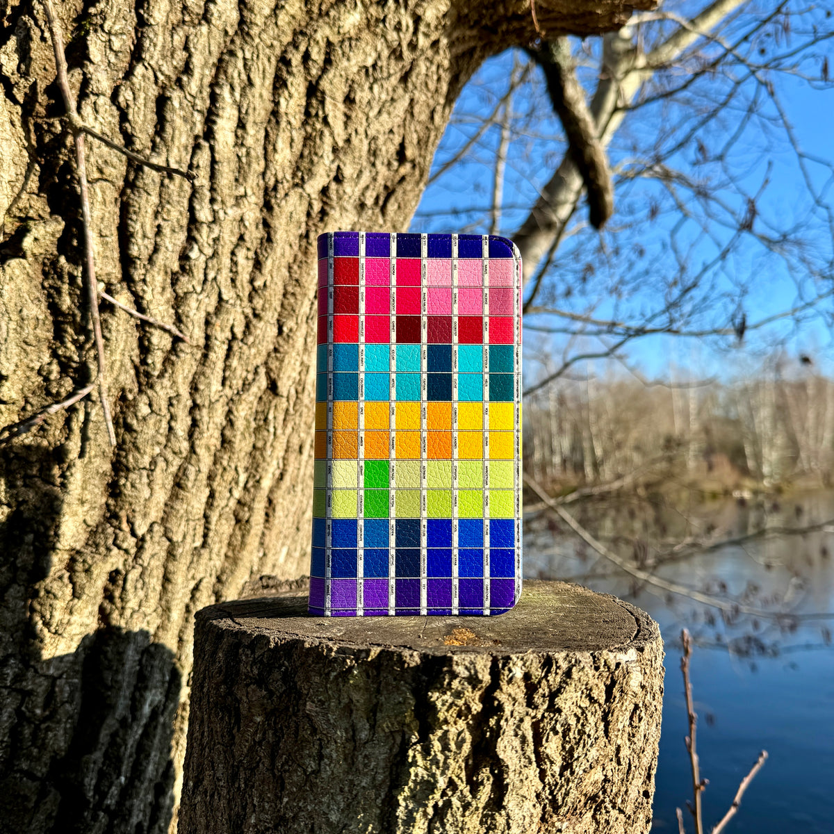 Chromology vegan leather wallet case with a colorful grid pattern, satin finish, and card slots, resting on a tree stump.