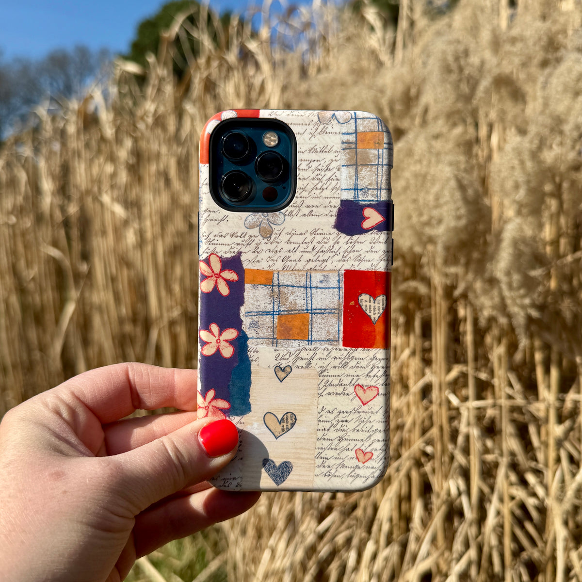 Alicia by Jehane iPhone tough case with a collage of vintage script, floral patterns, and hearts held against tall grass.