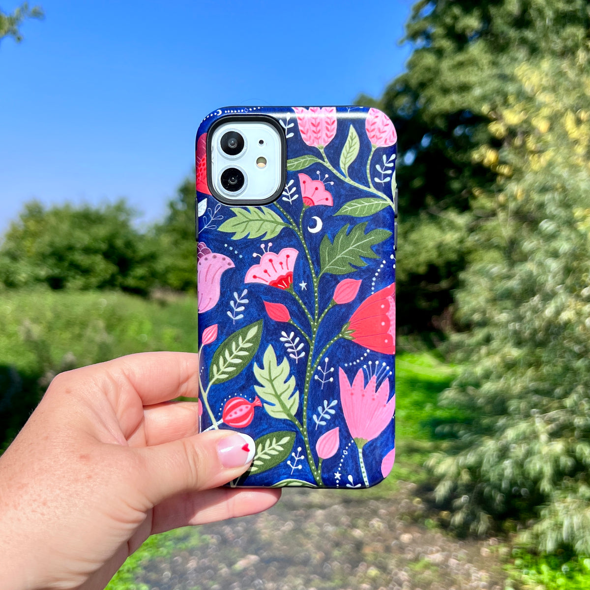 iPhone tough case featuring a blue floral pattern by Bex Parkin held against a blurred outdoor nature background.