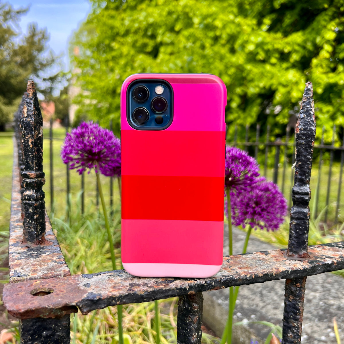 Ruby Grade iPhone Tough Case featuring horizontal stripes of pink and red on a dual-layer protective shell outdoors.