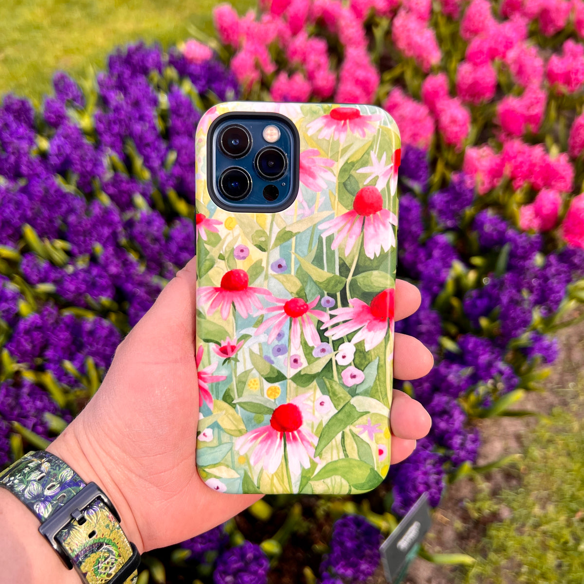 iPhone Tough Case featuring a vibrant Summer Echinacea floral print held against a background of purple and pink hyacinths.