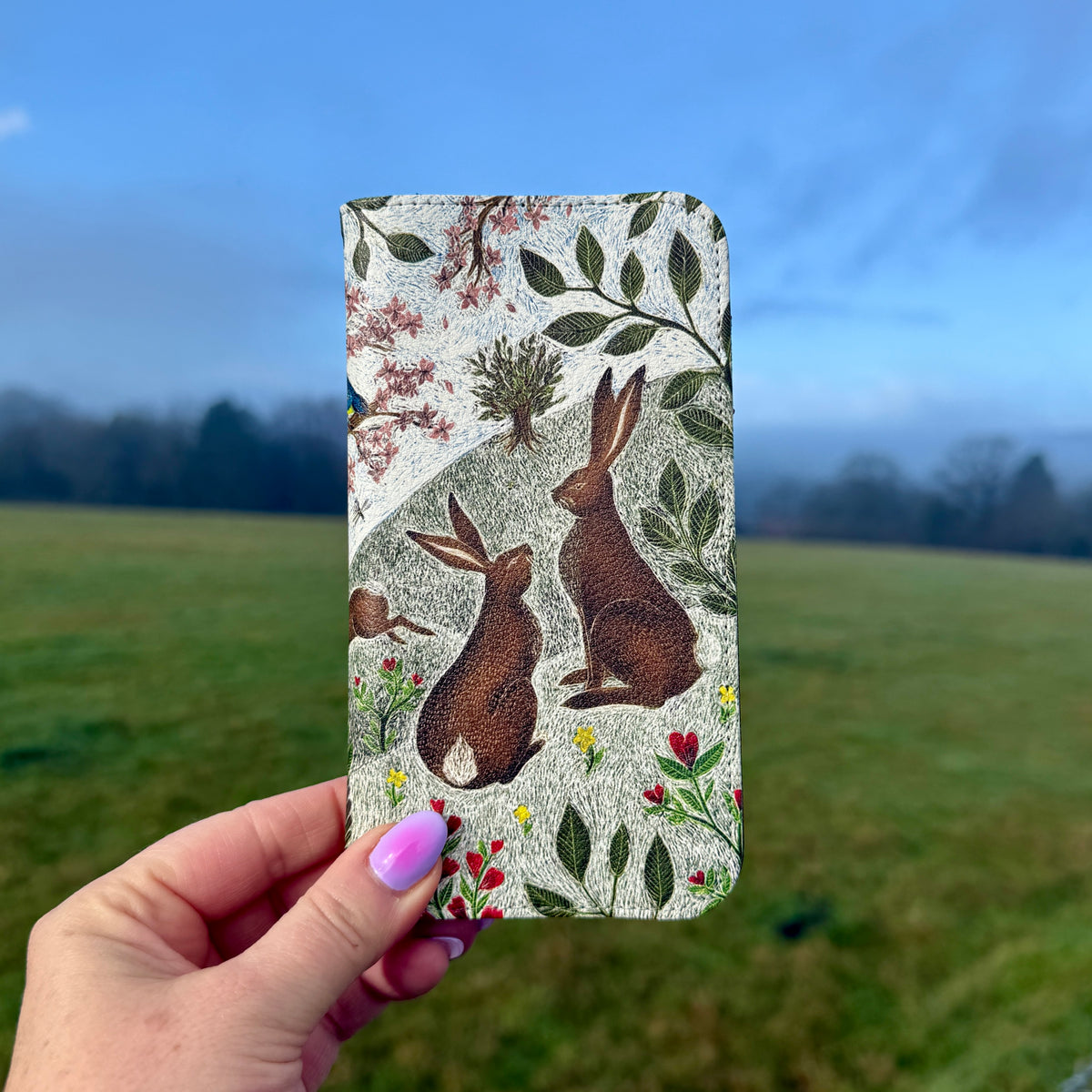 Vegan leather phone folio case featuring Sussex Downs rabbit artwork with a satin finish held against a green field.