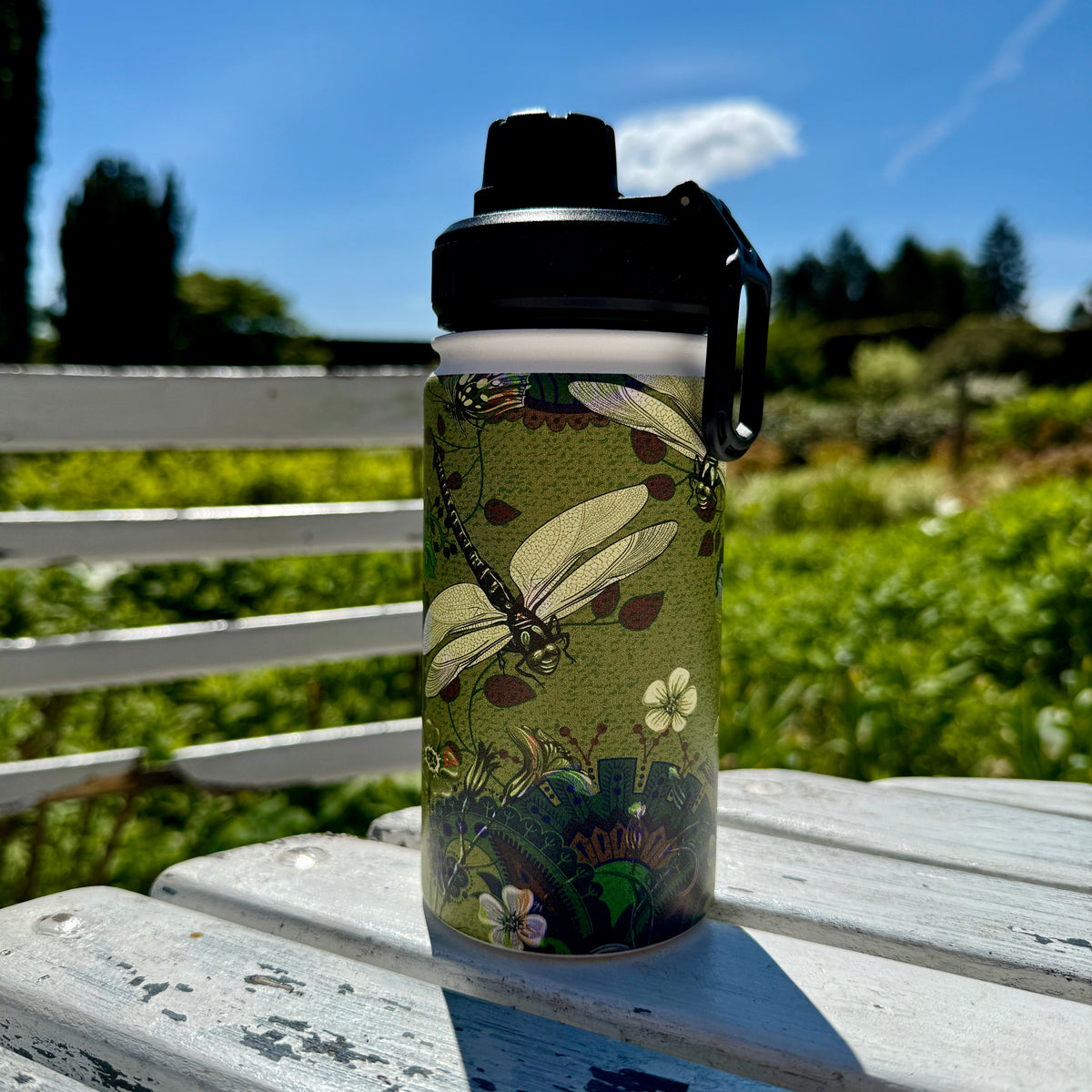 Vyne insulated stainless steel water bottle with a vibrant dragonfly and floral print on a white garden table.