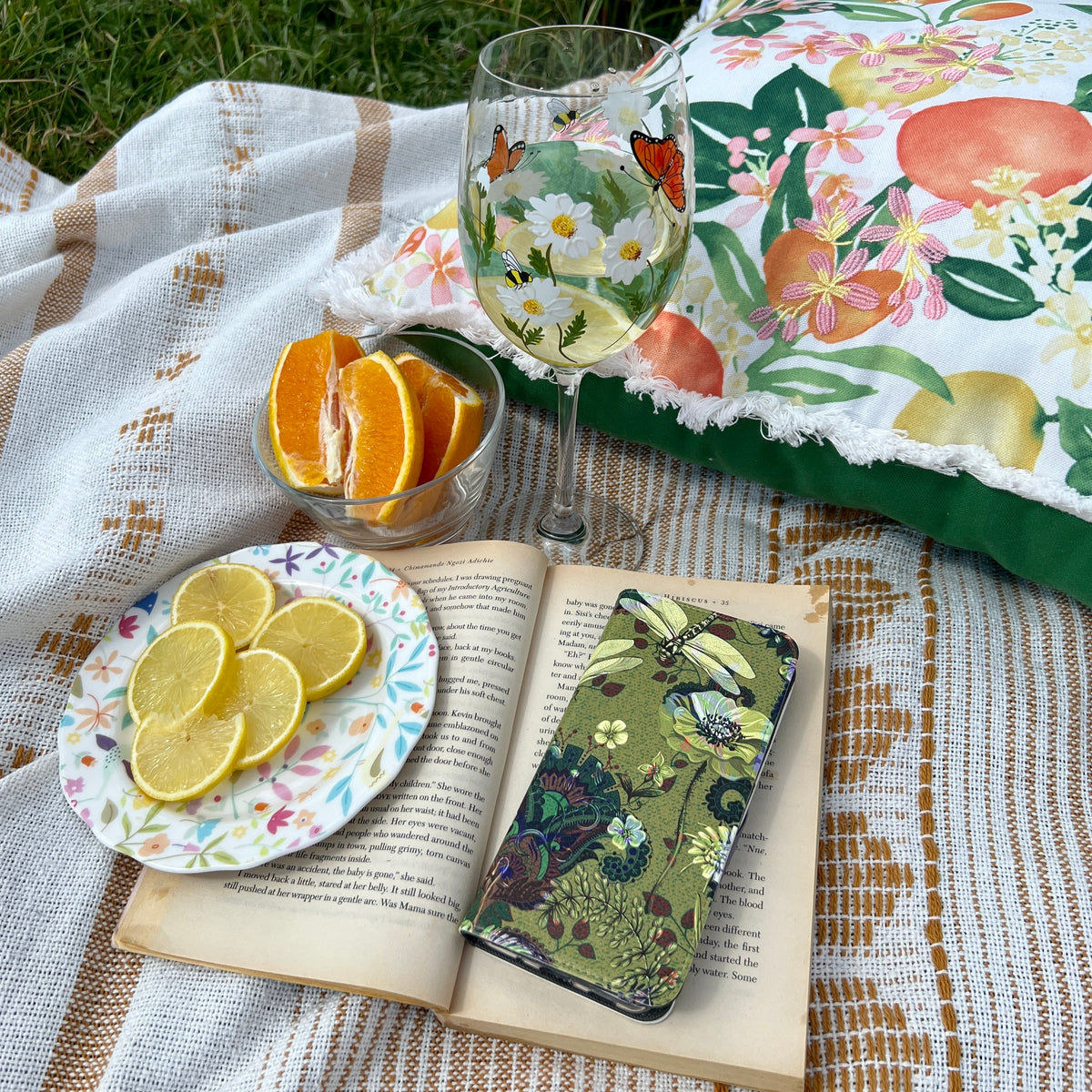 Vyne vegan leather folio case with green floral and dragonfly print resting on an open book during a picnic.