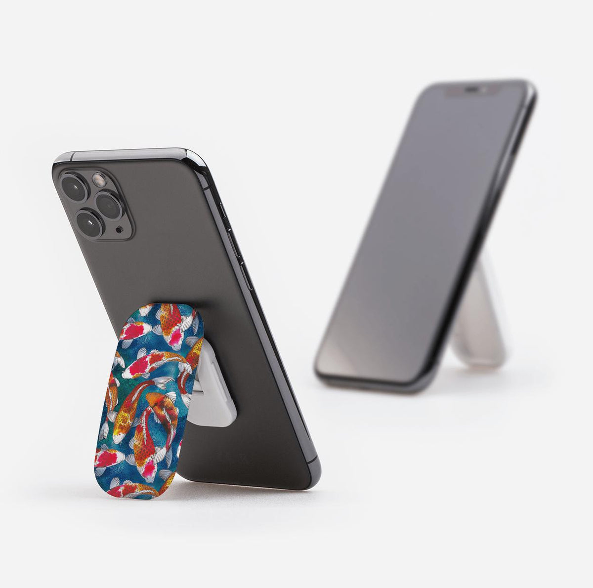Adachi phone stand with a colorful koi fish pattern attached to the back of a smartphone, propping it up on a white surface.