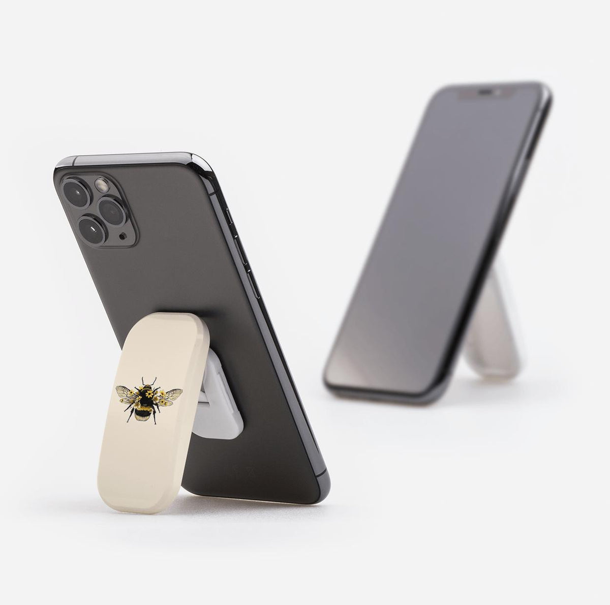 Cream-colored Clickit phone stand with a bumblebee illustration, attached to the back of a black smartphone as a kickstand.