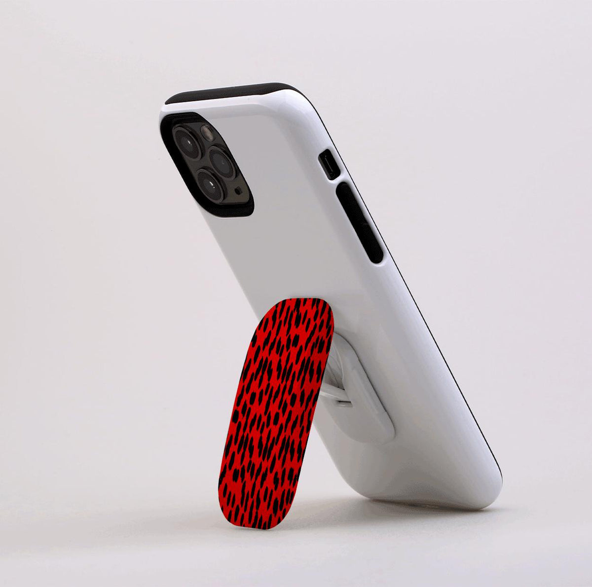 Black and red animal print Flickit phone stand attached to a white smartphone, propped up in landscape mode.
