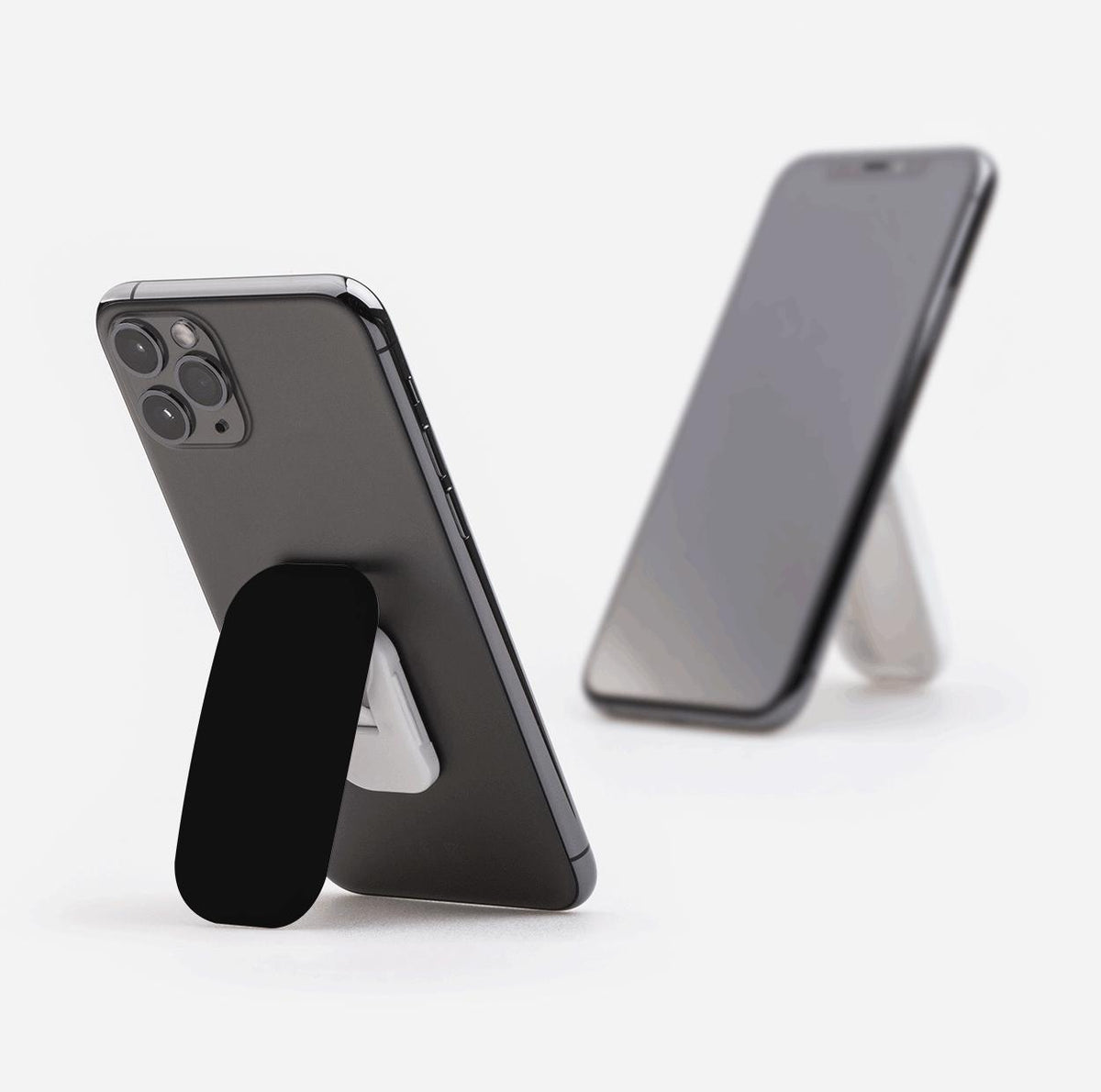 Black Flickit phone stand attached to a smartphone, functioning as a kickstand in portrait mode against a white background.