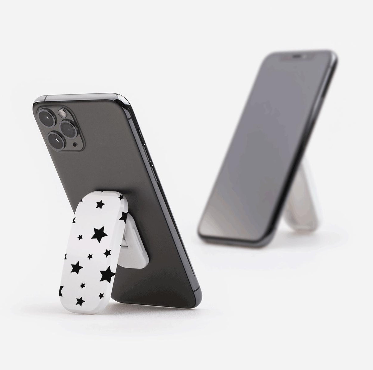 White Flickit phone stand with black star pattern attached to the back of a smartphone, propping it up on a white surface.