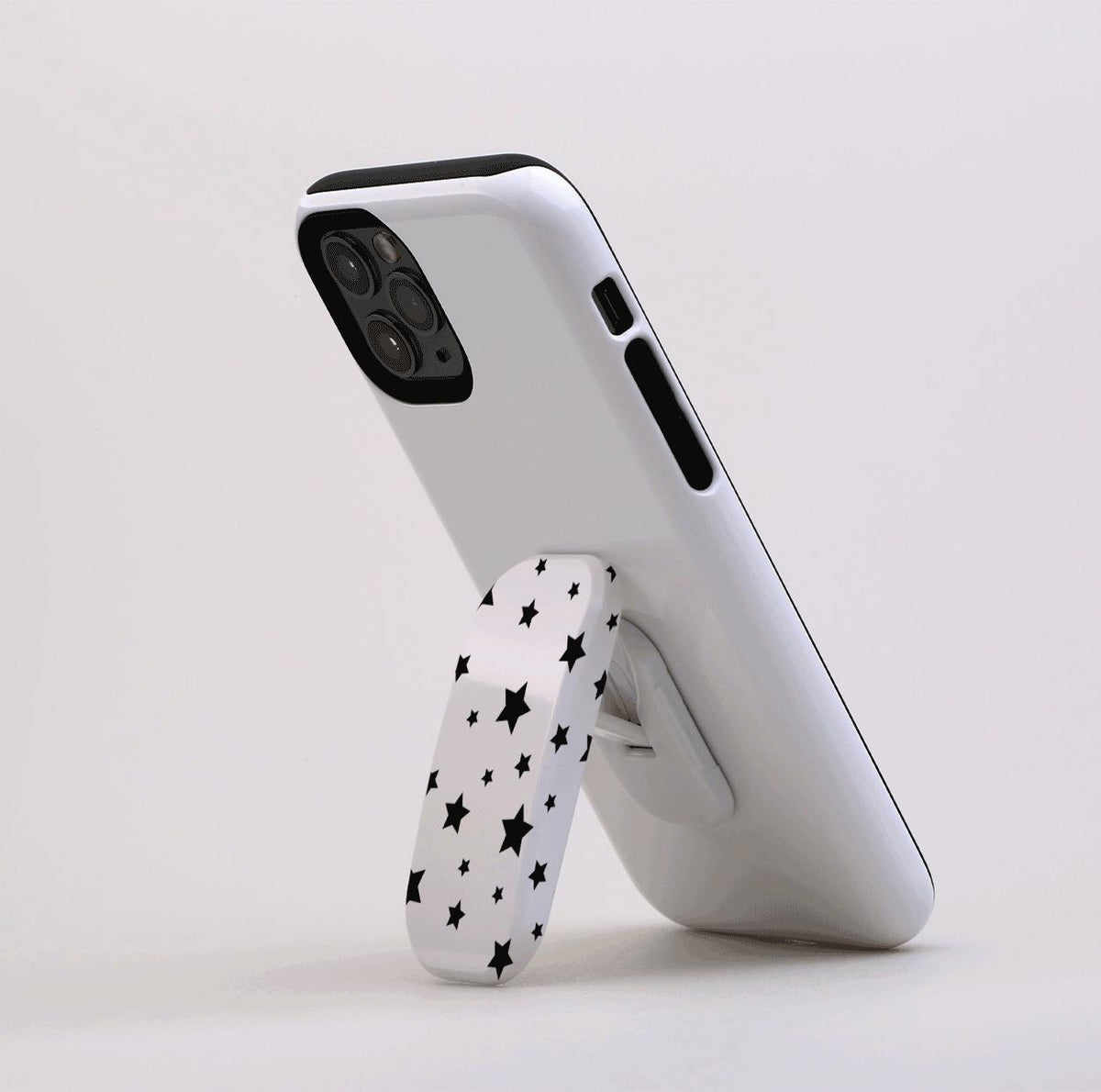 White phone case with a black star pattern Flickit stand propping up a smartphone on a white background.