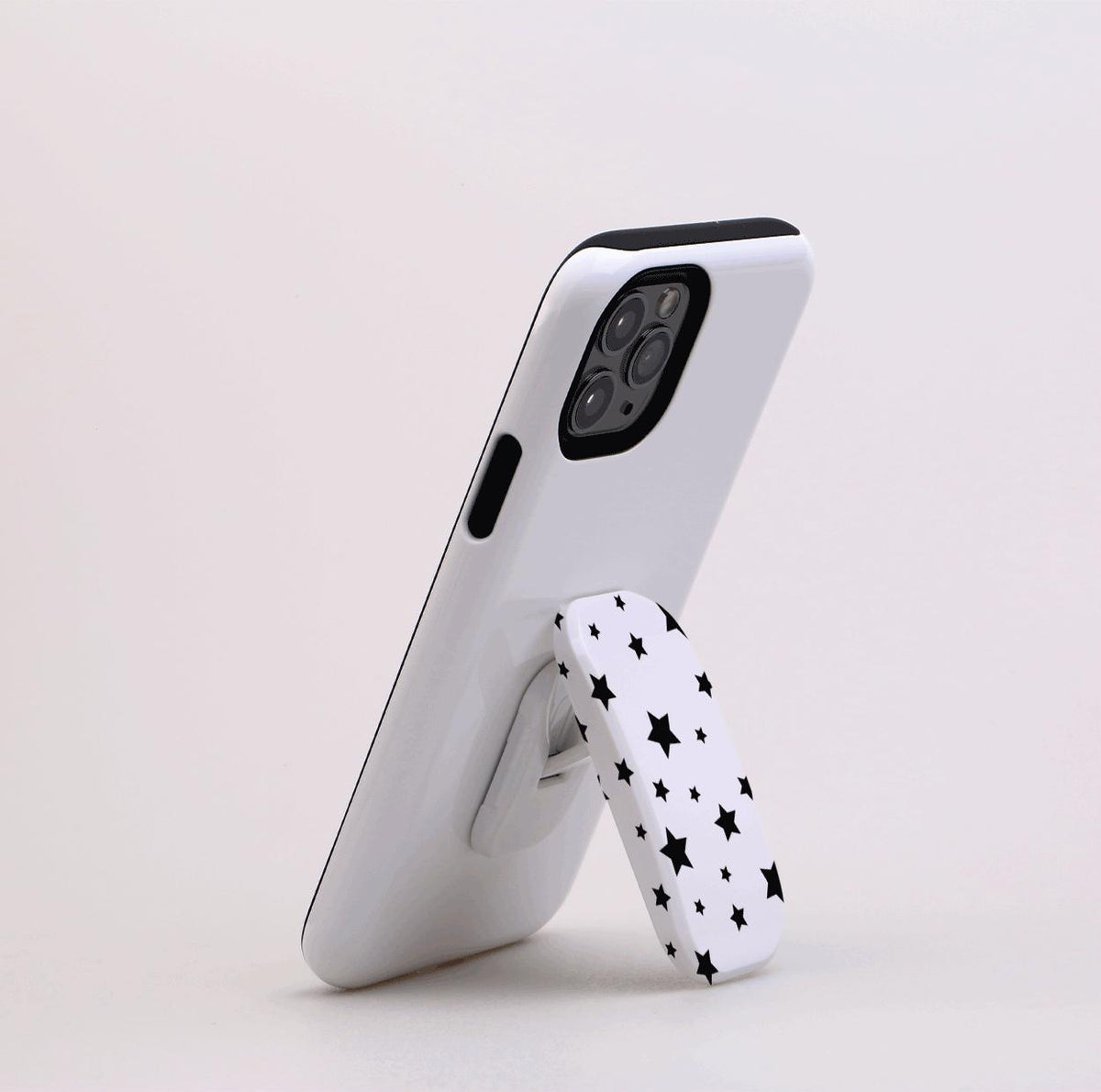 White smartphone propped up by a white Flickit stand featuring a black star pattern, shown in portrait mode.