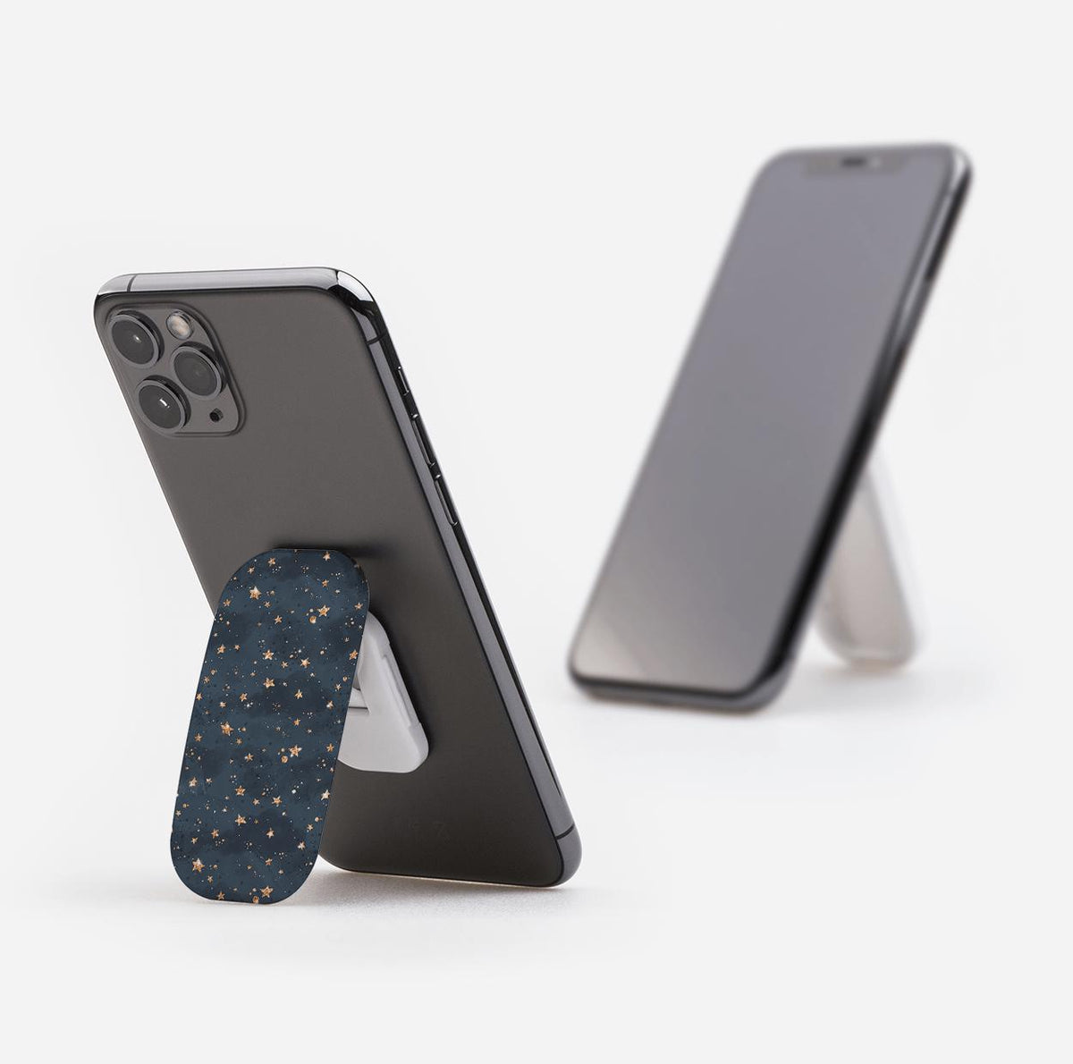 Bode Galaxy phone stand with a dark blue starry pattern, shown propping up two smartphones on a white background.