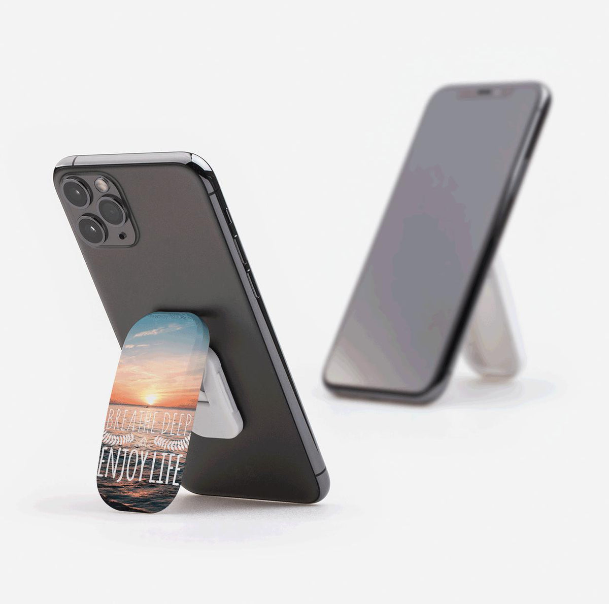 Breathe Deep Flickit phone stand with sunset ocean design, shown as a grip and a landscape stand on smartphones.
