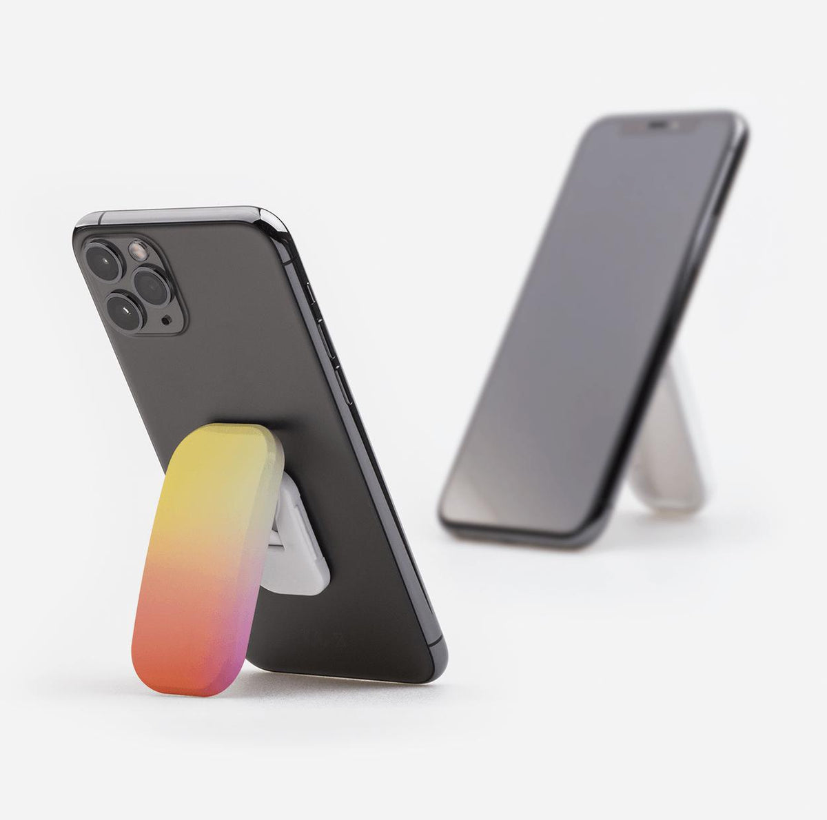 Chibo phone stand with a yellow-to-pink gradient finish attached to the back of a black smartphone on a white background.