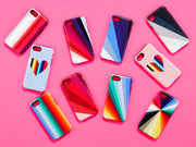 Collection of vibrant phone cases with geometric, rainbow, and heart patterns arranged on a bright pink background.