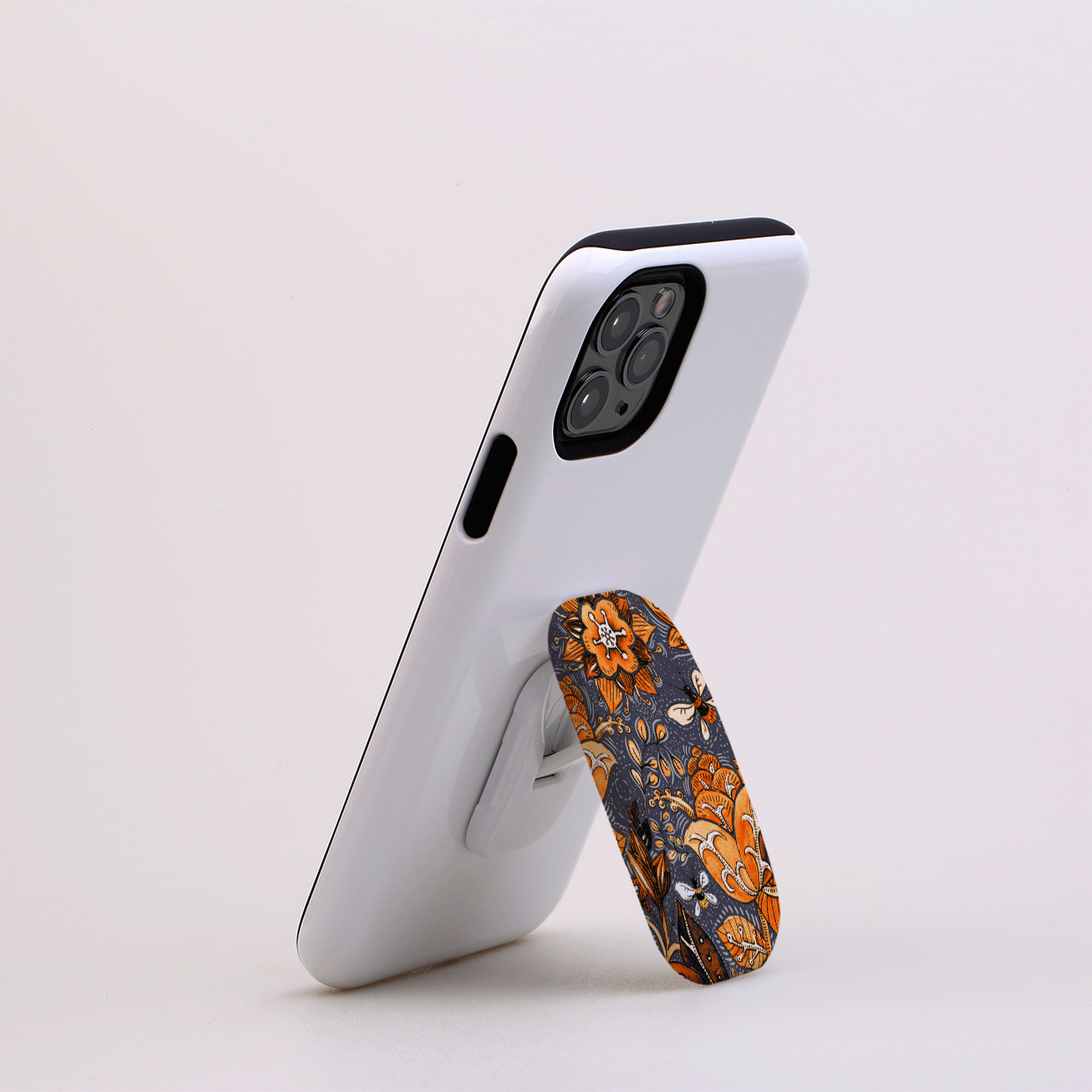 Hidcote Manor Flickit phone stand with an orange and grey floral pattern attached to the back of a white smartphone.