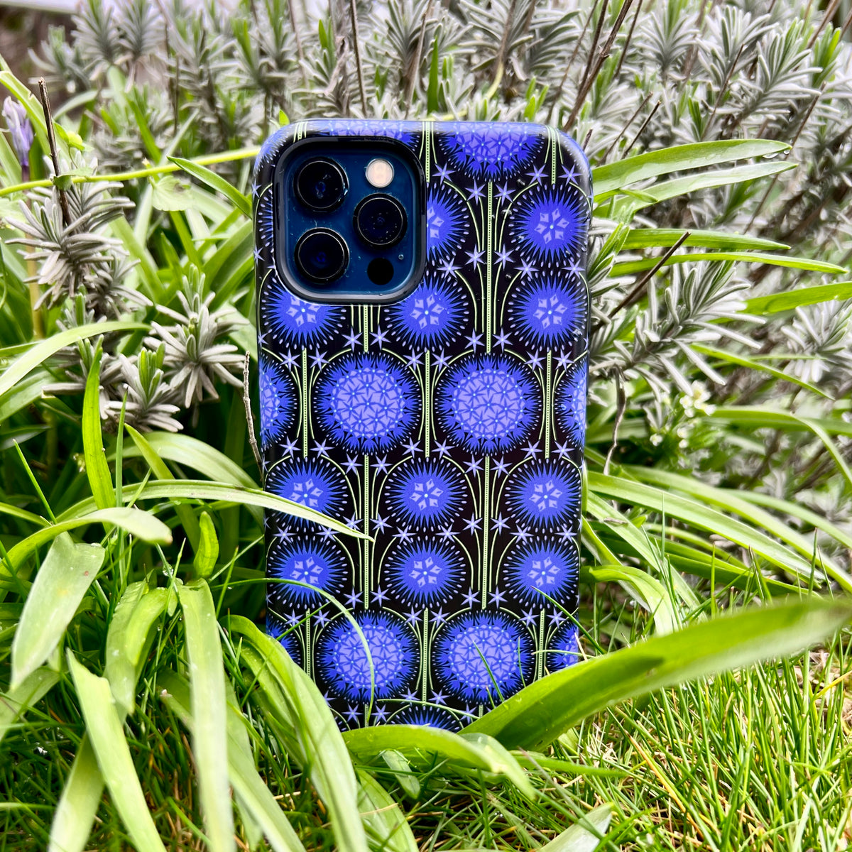 iPhone Tough Case featuring a blue and black Allium floral pattern by Cressida Bell, displayed in a lush garden setting.