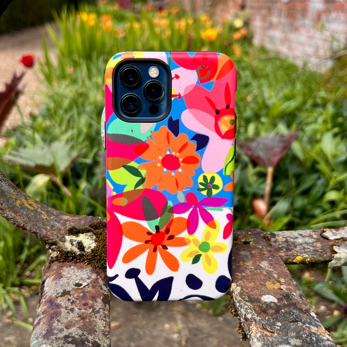 iPhone Tough Case featuring a vibrant, colorful floral pattern by Sarah Campbell, set against a blurred garden background.