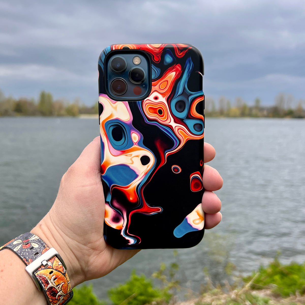 Butterscotch iPhone tough case with a vibrant, high-definition abstract swirl design held against a lake background.