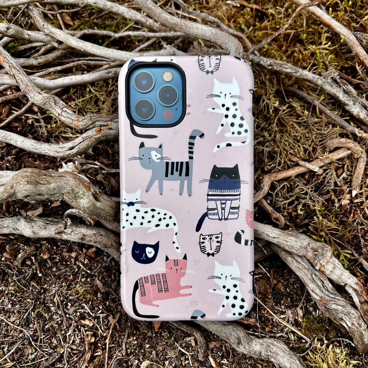 iPhone Tough Case featuring a whimsical cat pattern on a soft pink background, resting on a bed of twigs and moss.