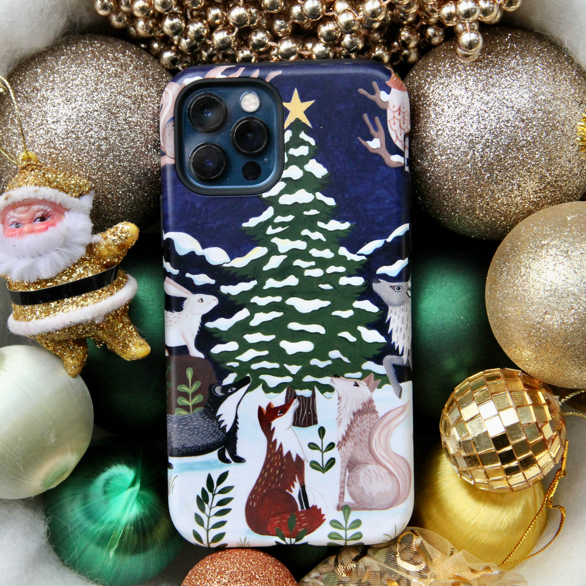 Dual-layer iPhone case featuring a festive Christmas tree and woodland animal illustration surrounded by holiday ornaments.