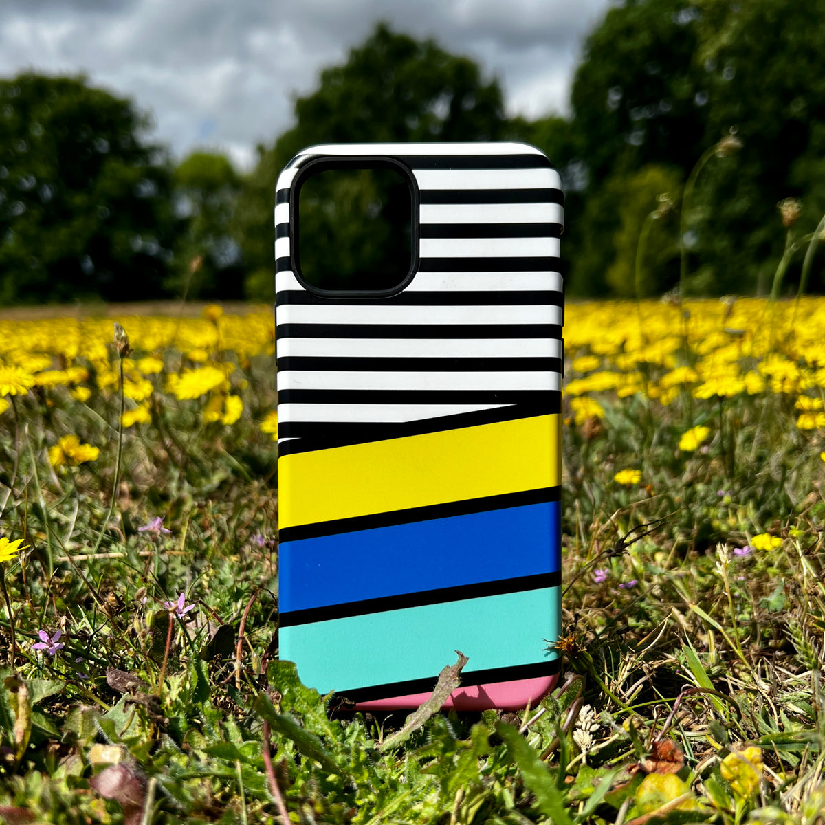 iPhone Tough Case with black and white stripes, yellow, blue, and teal color blocks standing in a field of yellow flowers.