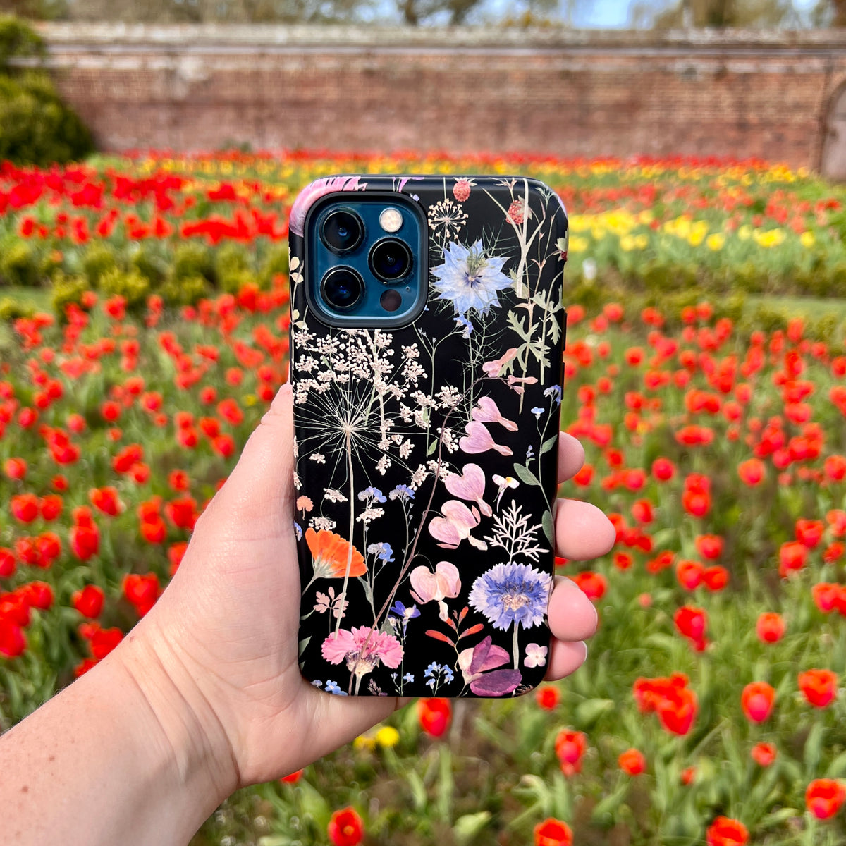 Hand holding a black iPhone tough case featuring a vibrant, high-definition pressed flower botanical print.
