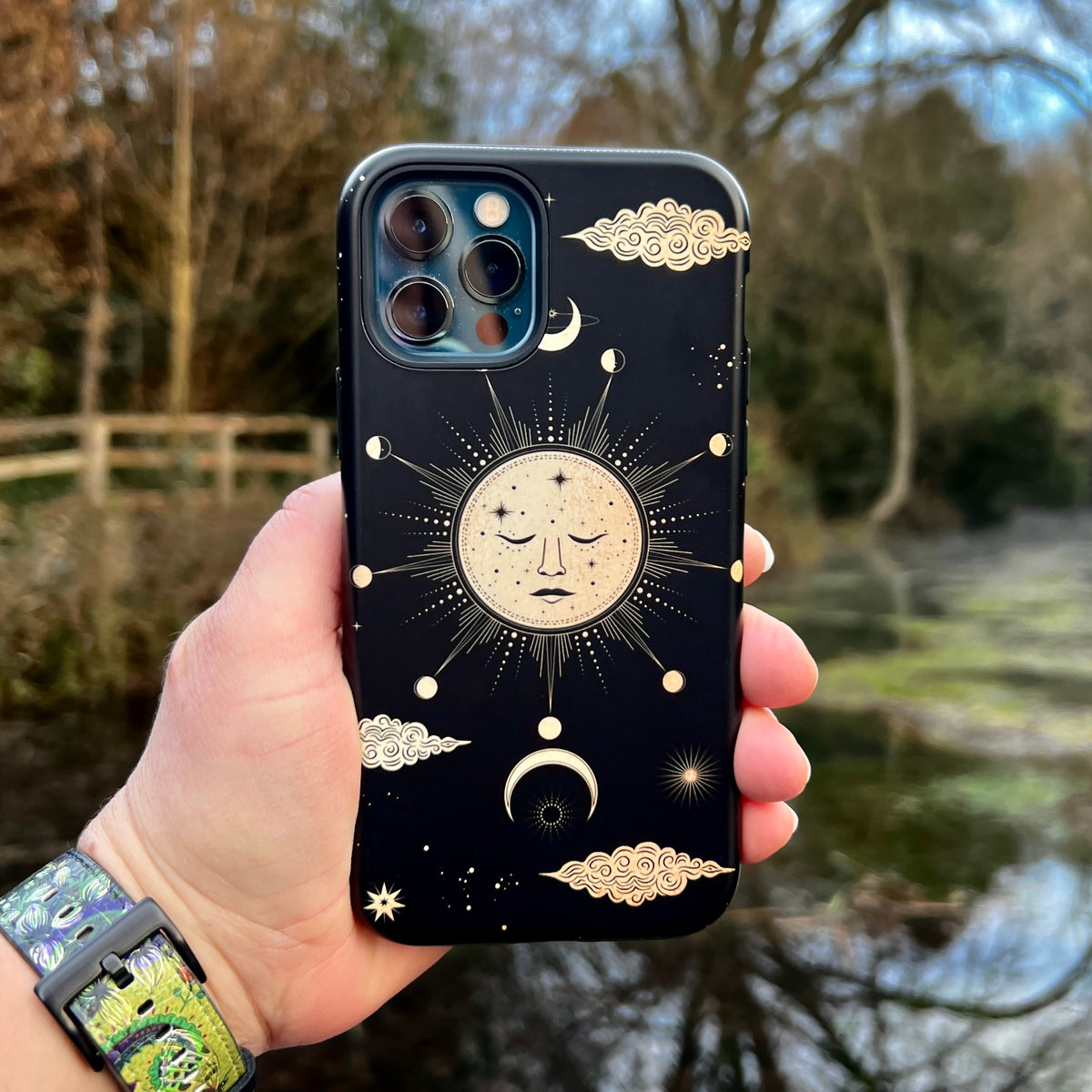 Black iPhone tough case featuring a celestial sun and moon design with gold stars and clouds against a dark background.