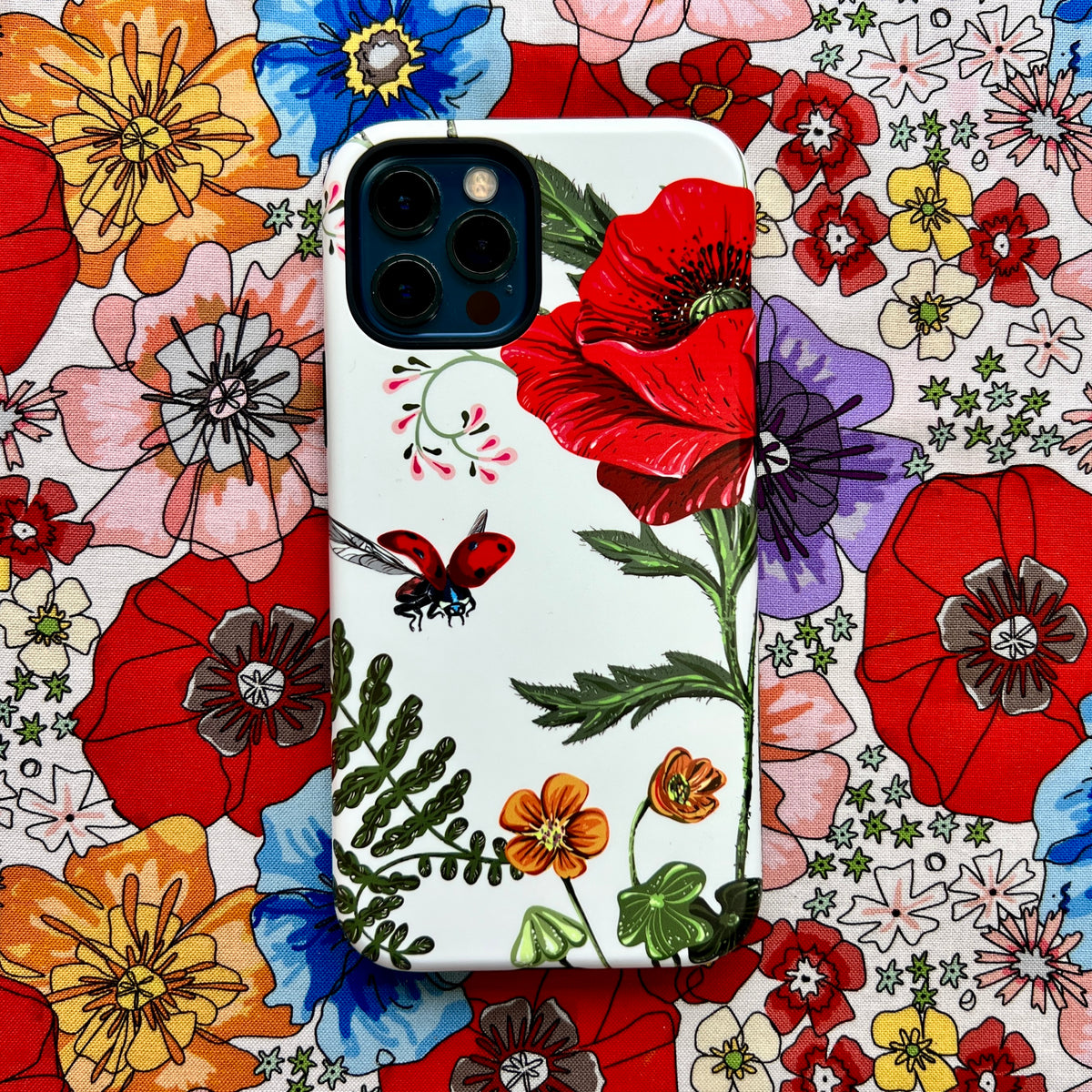 iPhone tough case featuring a vibrant red poppy and ladybug floral design on a white background against a matching fabric.