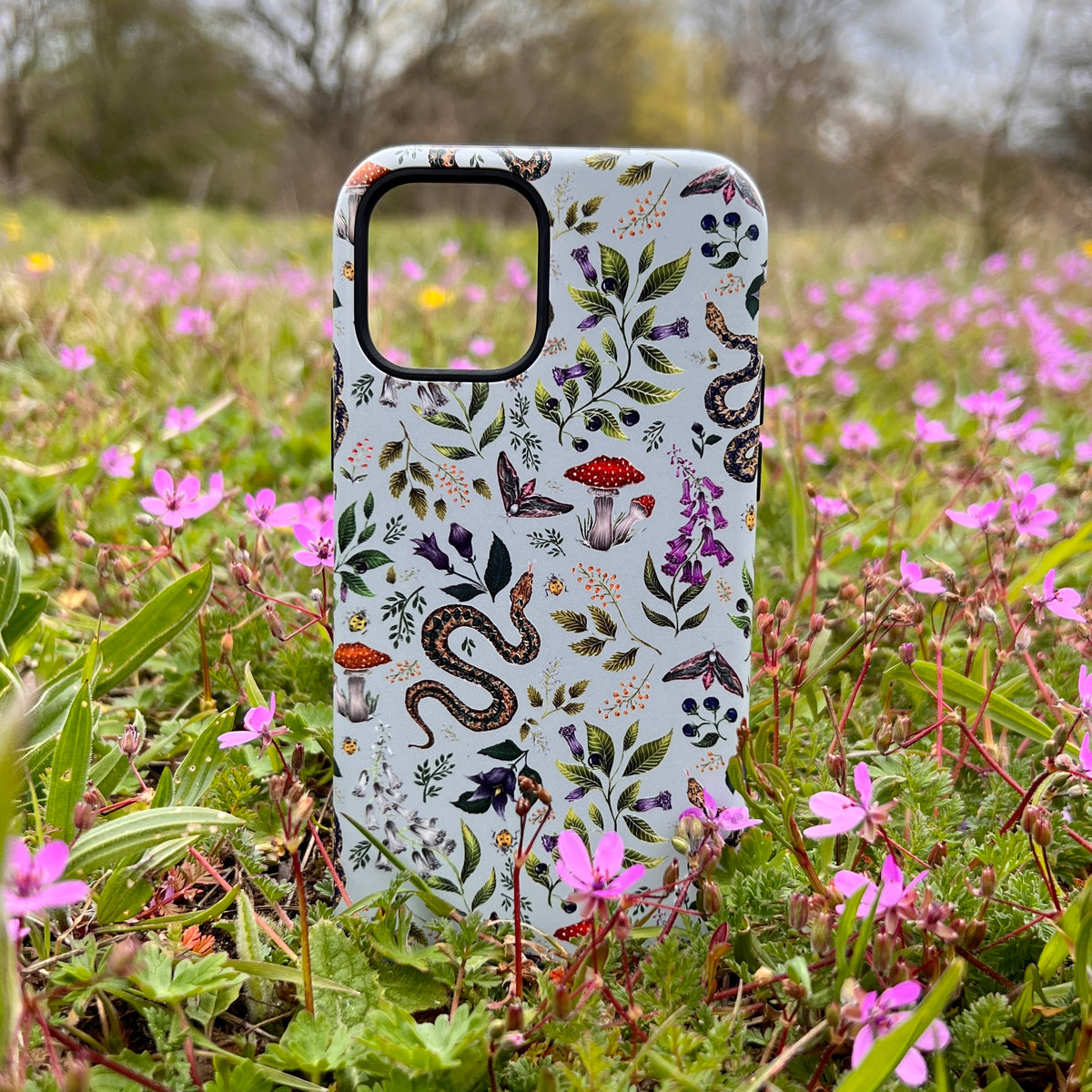 iPhone tough case featuring Catherine Rowe’s Poisonous 2 snake and mushroom botanical print, standing in a field of flowers.
