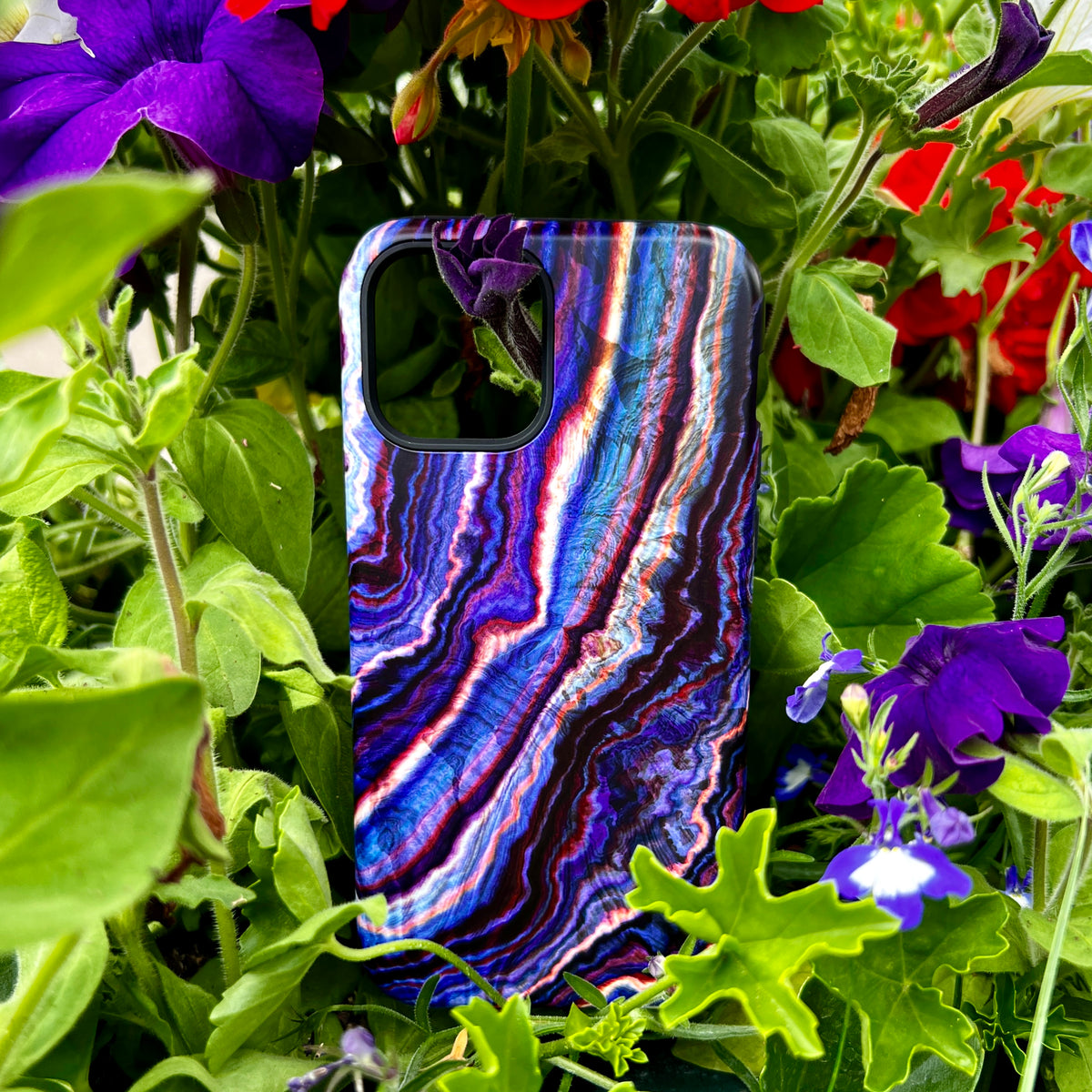 Royal Agate iPhone tough case with a dual-layer design and vibrant blue, purple, and white marbled pattern in a garden.
