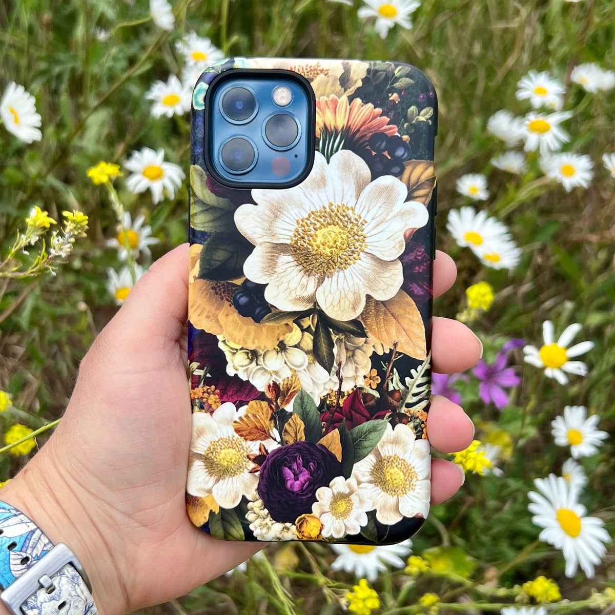 iPhone Tough Case with a vibrant floral Surreal print held against a background of white daisies and wildflowers.