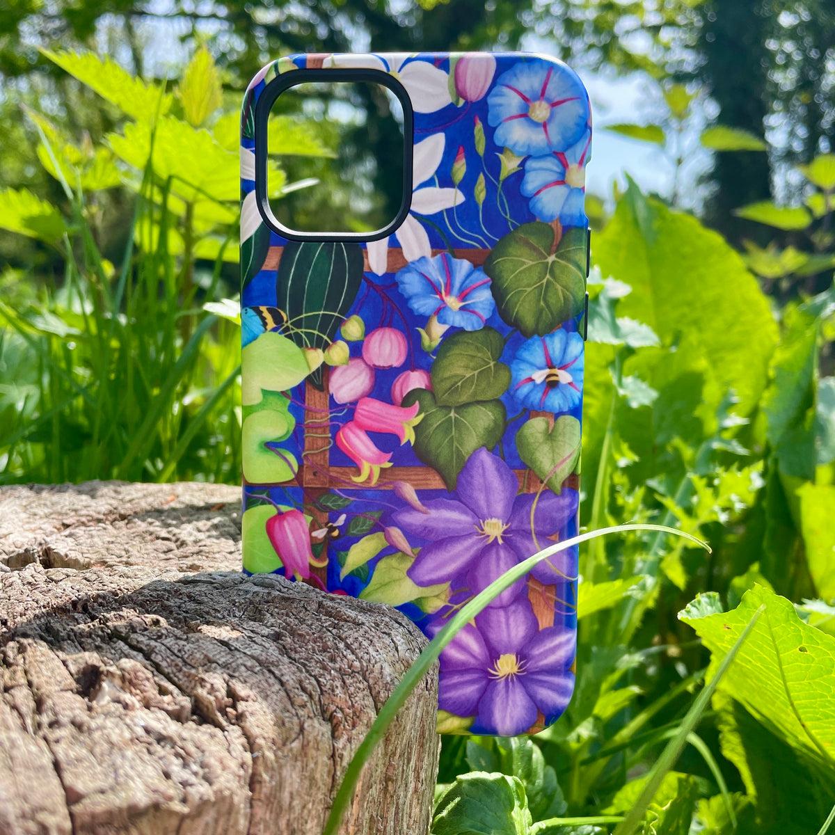 iPhone Tough Case featuring Bex Parkin’s colorful floral trellis artwork on a wooden stump outdoors.