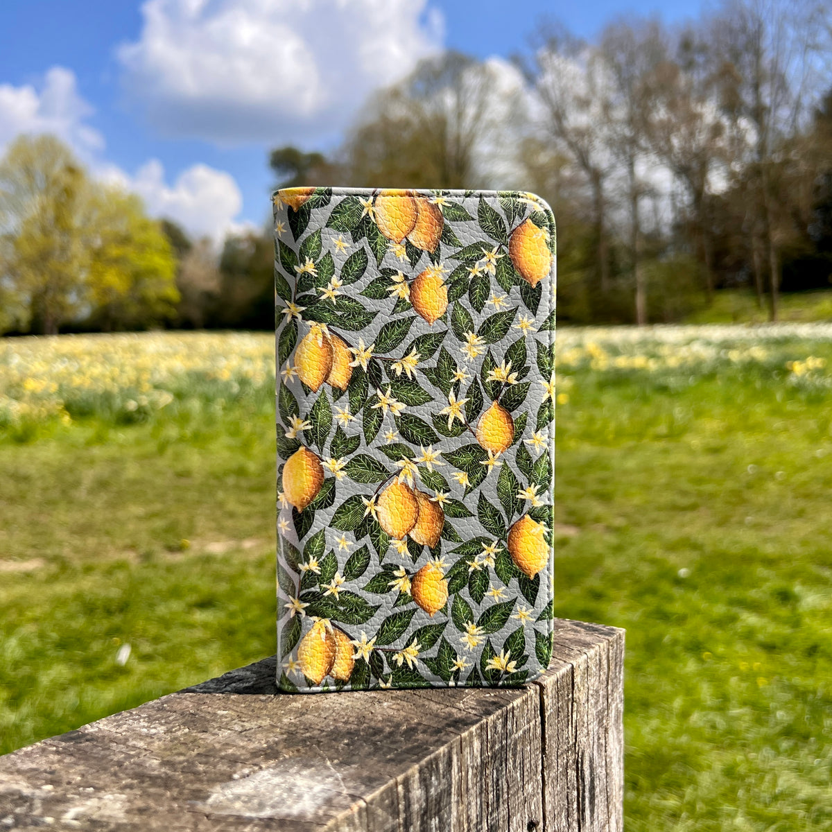 Vegan leather phone folio case with a satin finish featuring a yellow lemon and green leaf pattern on a grey background.