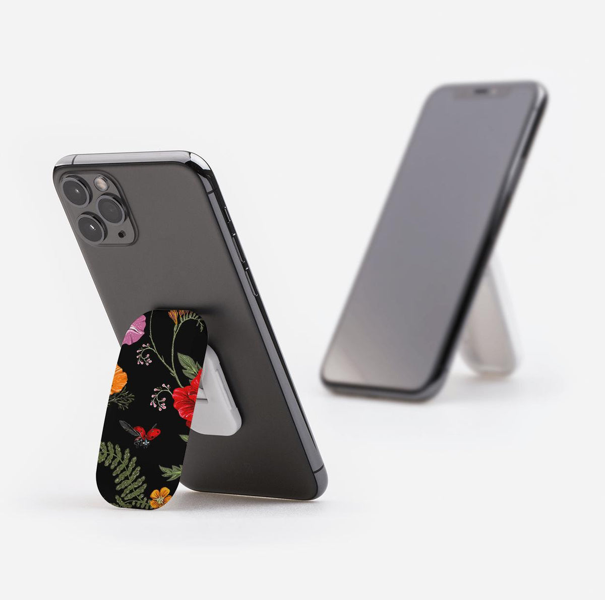 Moonlight Garden phone stand with floral and ladybug print attached to the back of a black smartphone.