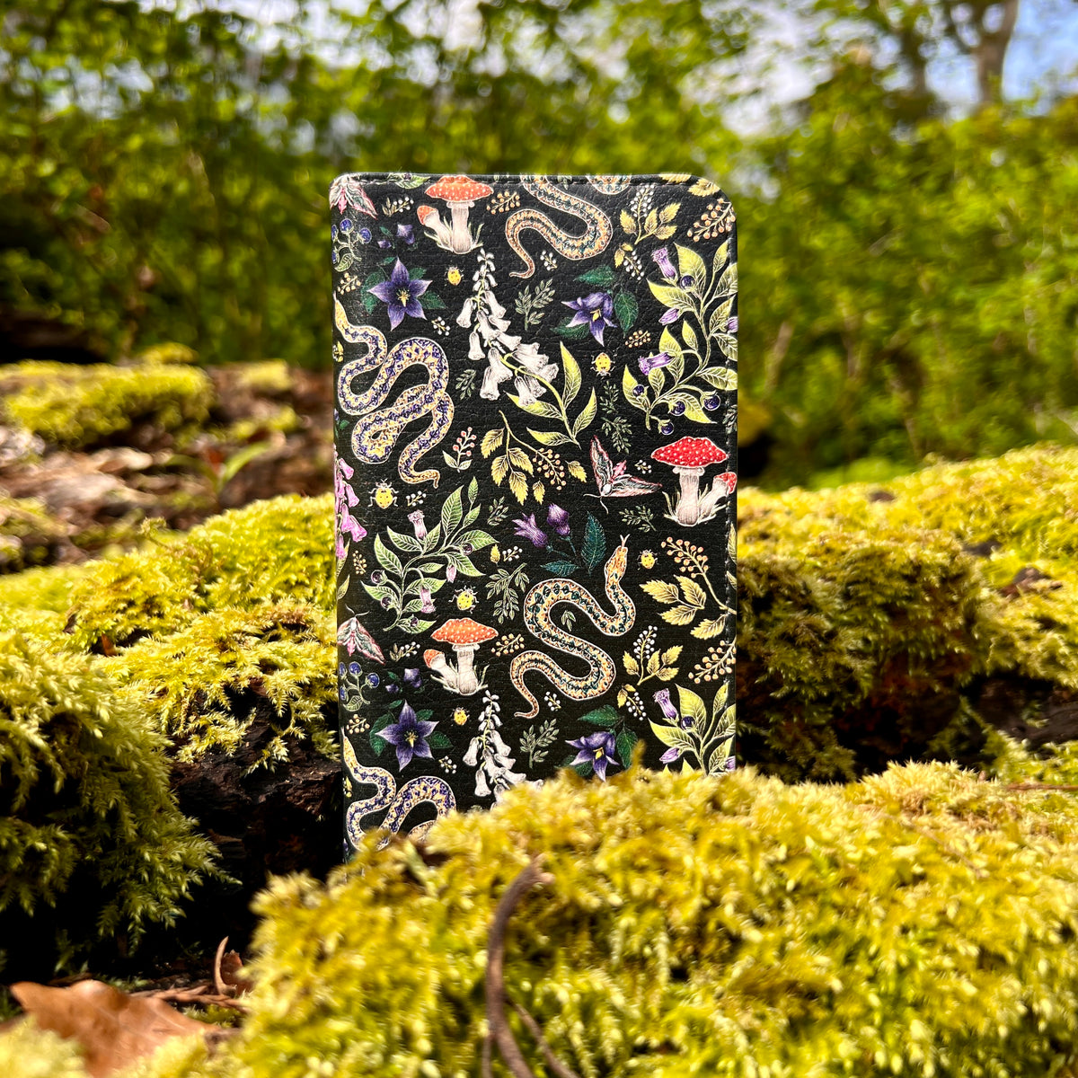 Vegan leather folio phone case with Poisonous snake and mushroom botanical print in a satin finish on mossy ground.