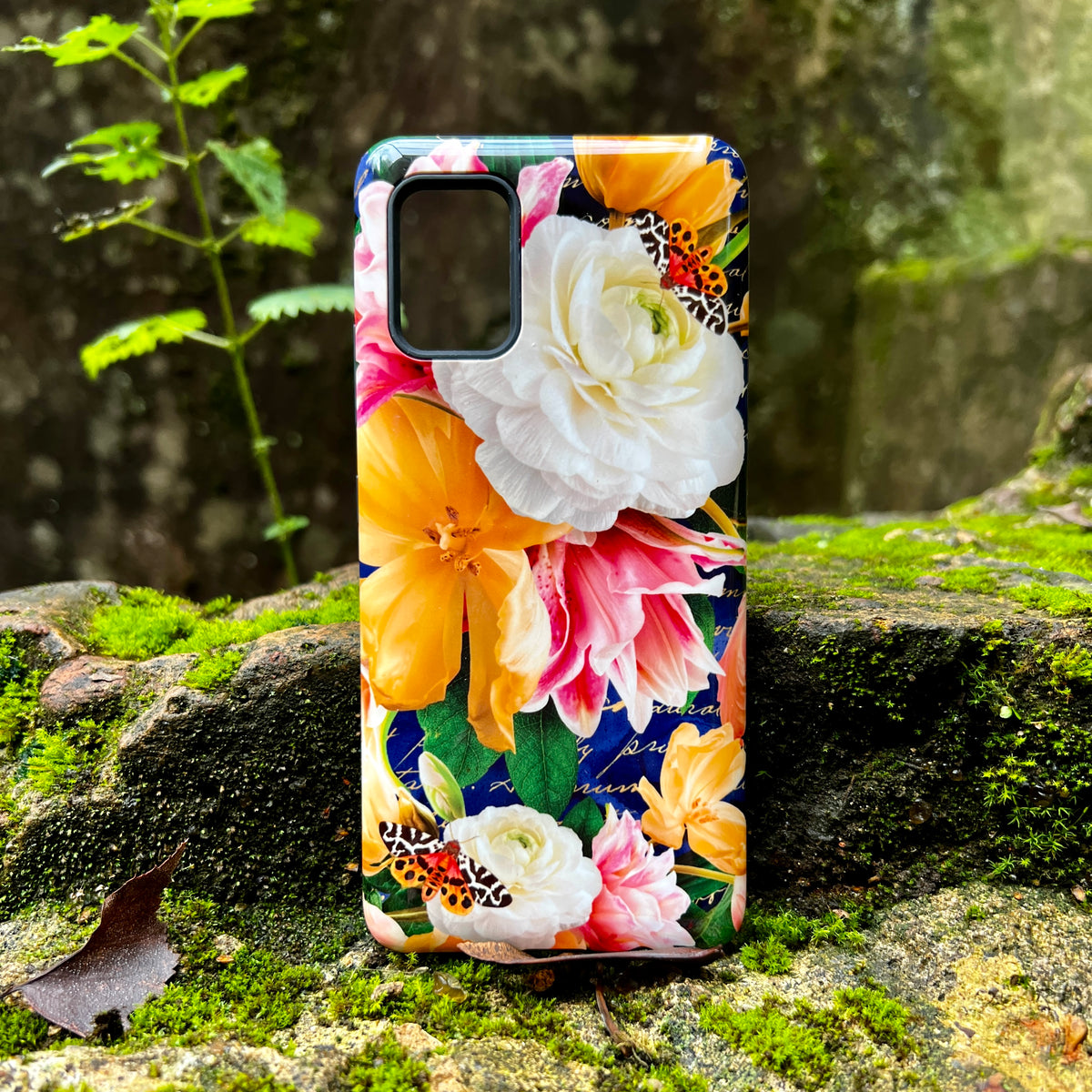 Samsung Tough Case with vibrant floral and butterfly print on a dual-layer protective shell resting on mossy stone.