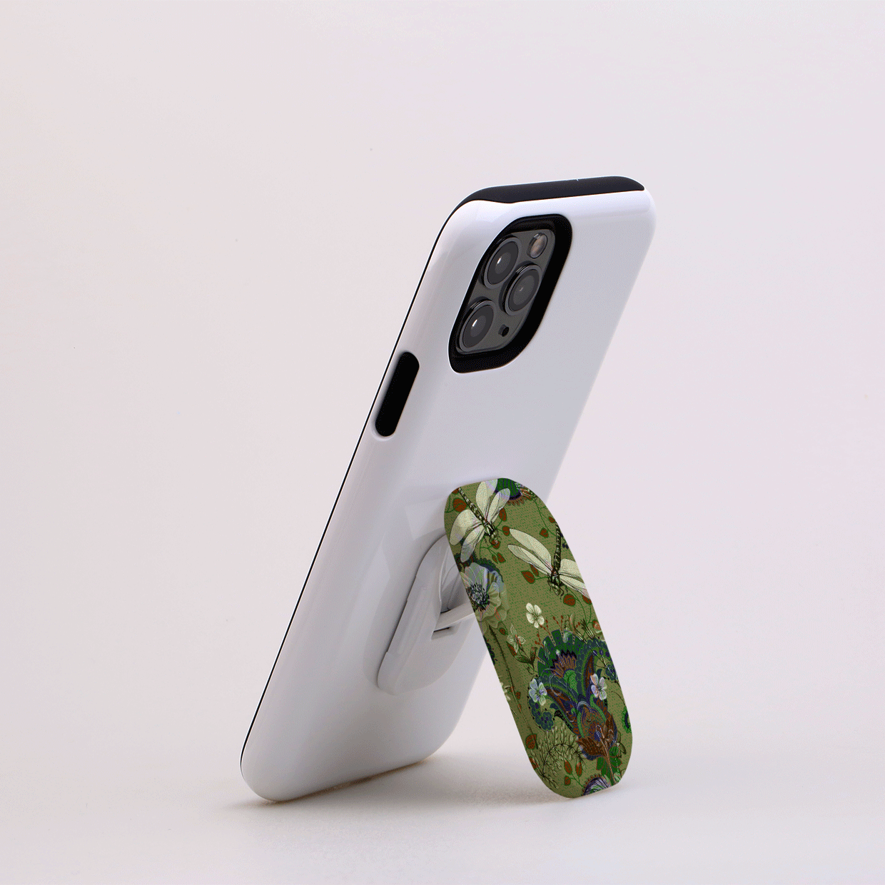 White smartphone propped up by a green, dragonfly-patterned Flickit stand in portrait mode on a plain background.