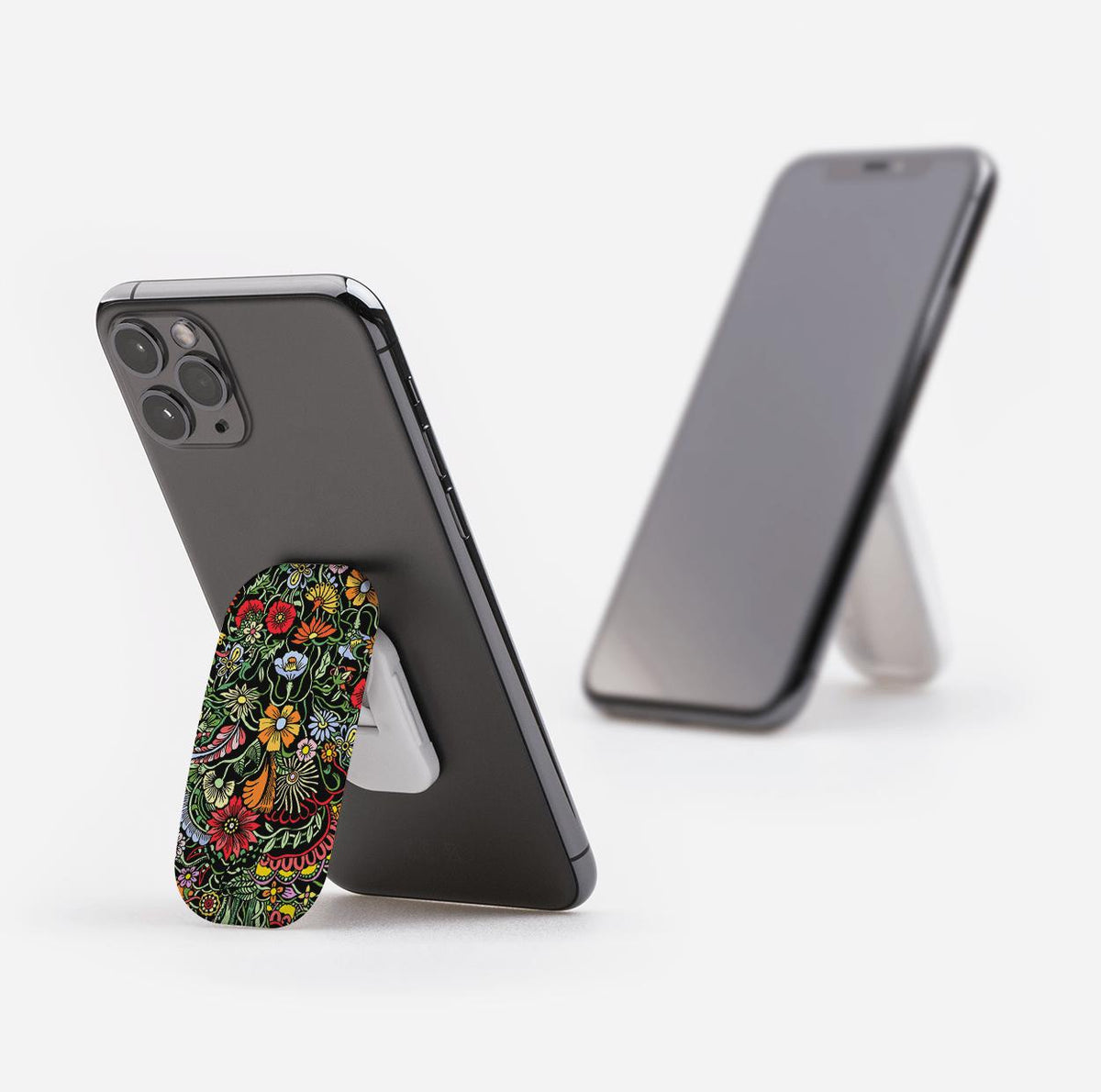 Verona phone stand with a colorful floral pattern attached to the back of a black smartphone, propping it up on a white surface.