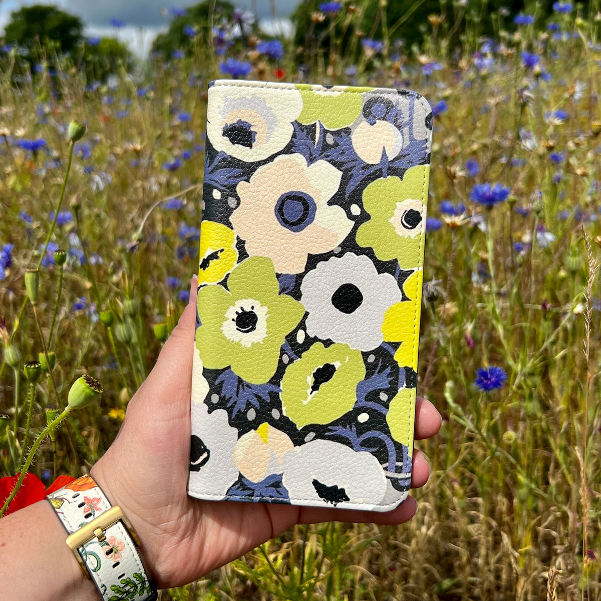 Vegan leather phone folio case with Windflowers Urbane floral print in green, white, and navy against a wildflower field.